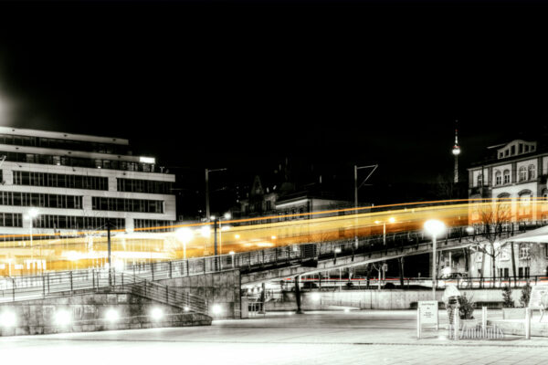 Der Lichtschweif einer Zahnradbahn am Marienplatz. Bild in Schwarzweiss mit gelbem Lichtschweif.