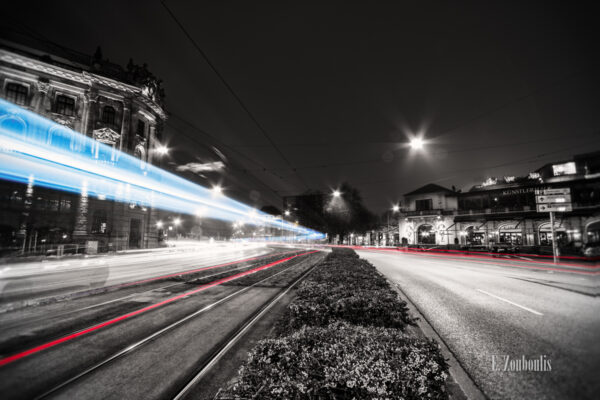 Schwarzweiss-Aufnahme am Lenbachplatz in München. Rote und blaue Lichtschweife sind zu sehen.