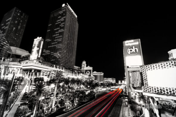 Schwarzweiss-Aufnahme am Las Vegas Strip mit roten Lichtschweifen, die den Verkehr an der Hauptader der Stadt erkennen lassen. Rechts das Planet Hollywood Casino und auf der Linken seite das Cosmopolitan vor dem Bellagio Casino