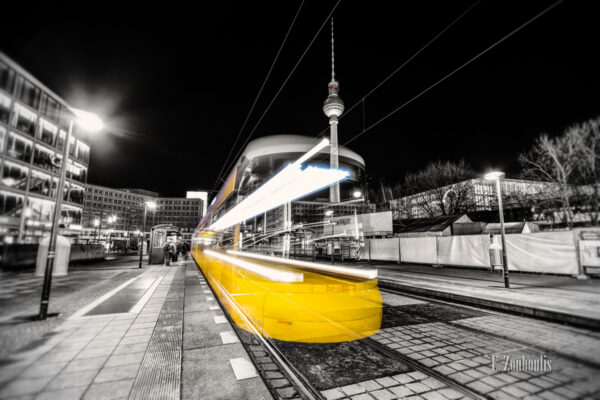 Schwarzweiss-Aufnahme einer einfahrenden Straßenbahn am Alexanderplatz in Berlin. Schwarzweiss mit farbigem Lichtschweif, der die Straßenbahn erkennen lässt