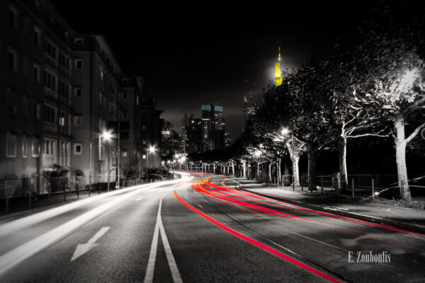 Schwarzweiss-Aufnahme in Frankfurt Sachsenhausen mit rotem Lichtschweif des Verkehrs und farbigen Elementen im Hintergrund, die dem Bankenviertel entspringen