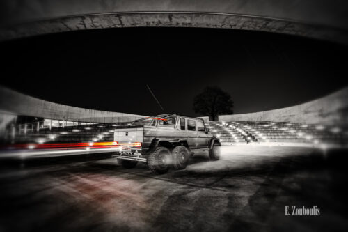 Schwarzweiß-Aufnahme eines Mercedes Benz G63 6x6 AMG in der Arena des Mercedes Benz Museums in Stuttgart. Ein roter Lichtschweif ist an den Rücklichtern des Fahrzeugs zu sehen