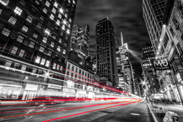 Schwarzweiss-Aufnahme in New York City. Rote Lichtschweife kennzeichnen den Verkehr. Auf dem Gehweg wurde der Müll abgeladen.