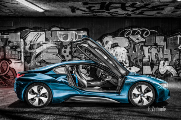 Schwarzweiss-Aufnahme mit einem blauen BMW i8 mit geöffneten Flügeltüren vor einer Graffiti Wand