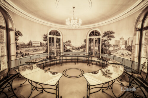 Sepia Aufnahme in der Villa Schwalbenhof. Glastische und Sitzbänke im Kreis unterhalb eines Kronleuchters und schönen Wandbildern