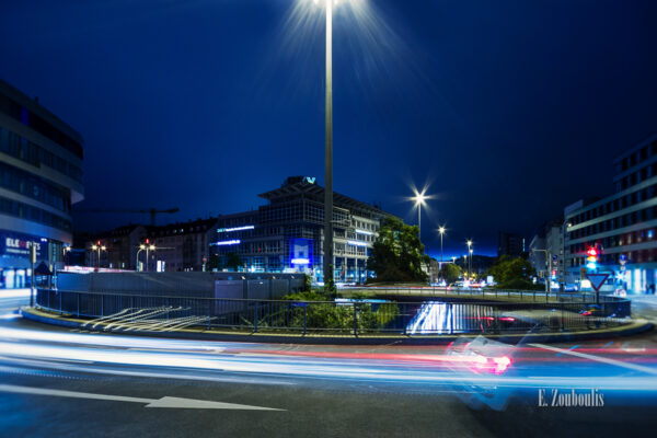 Nachtaufnahme am Österreichischen Platz in Stuttgart. Im Hintergrund sind die letzten Strahlen des Tageslichts zu sehen und im Vordergrund der Verkehr in Form von Lichtschweifen, die sich entlang des Kreisverkehrs und der B14 schlängeln