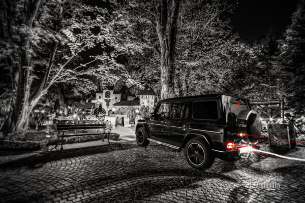 Schwarzweiß-Aufnahme eines Mercedes G63, der im Europa Park einen roten Lichtschweif hinterlässt vor einem Märchen-Häuschen