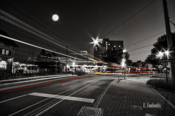 Schwarzweiß-Aufnahme am Vaihinger Bahnhof mit vorbeiziehendem Bus in Form roter und gelber Lichtschweife im Vordergrund des Pullman Hotel und des Vollmonds