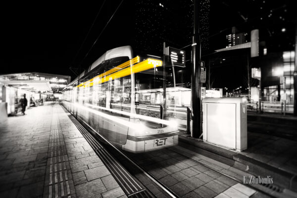 Schwarzweiß-Aufnahme einer rasenden Tram in Rotterdam. Ein Geisterzug, der einen gelben Lichtschweif hinter sich her zieht