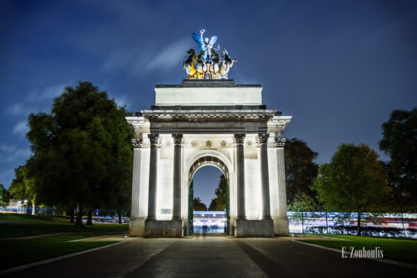 Abendaufnahme am Greeen Park in London, Großbritannien. Die Menschen laufden durch den Wellington Arch hindurch. Im Hintergrund hinterlässt der Verkehr Lichtschweife