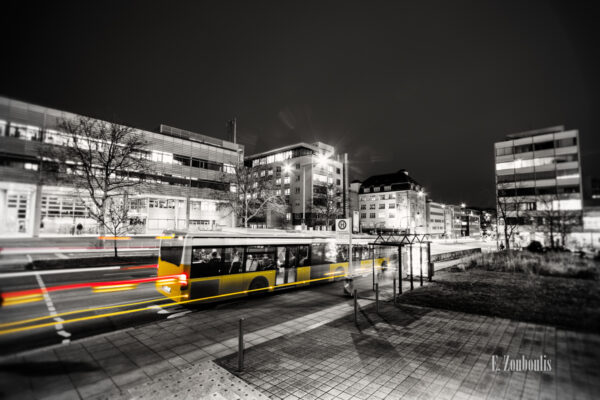 Schwarzweiß Aufnahme vor dem Katharinenhospital in Stuttgart. Ein gelber "Geisterbus" hinterlässt rote und gelbe Lichtschweife beim einfahren in die Haltestelle