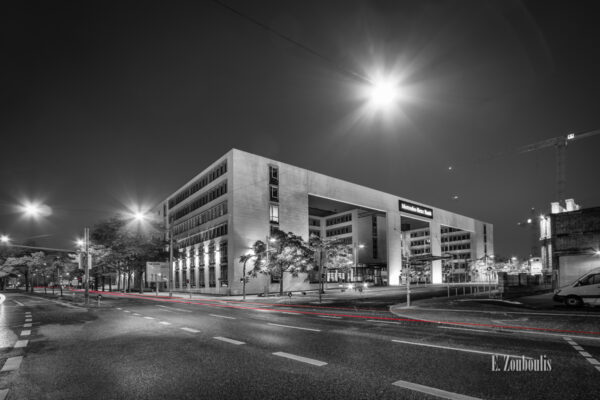 Schwarzweiß Aufnahme vor dem Gebäude der Mercedes Benz Bank am Pragsattel, Stuttgart. Im Vordergrund ist ein roter Lichtschweif zu sehen, der den Verkehr erkennbar macht