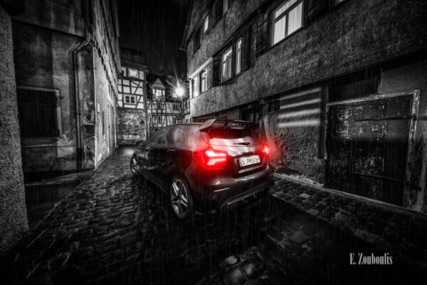 Nachtaufnahme in Schwarzweiß mit roten Heckleuchten einer schwarzen Mercedes AMG A-Klasse. Im Vordergrund der AMG auf nassem Pflasterstein. Im Hintergrund die Fachwerkhäuser in einer kleinen Gasse in Tübingen. Bild aufgenommen auf Einladung von Mercedes Benz