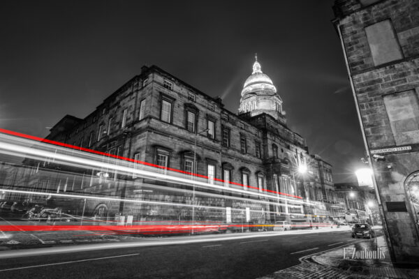 Langzeitaufnahme vor der University of Edinburgh, Schottland mit einem roten Lichtschweif, der den Verkehr nachts vor der Universität sichtbar macht