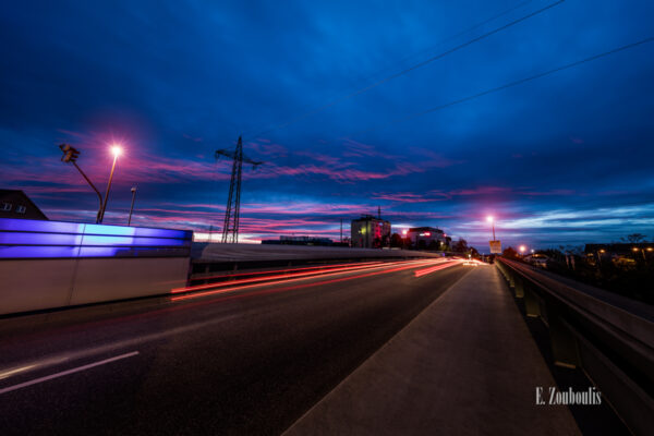 Zur Abenddämmerung in Böblingen. Auf der Brücke der Calwer Straße hinterlassen die vorüber fahrenden Autos rote Lichtschweife. Die Wolken bekommen von der untergehenden Sonne eine rötlich / pinke Farbe