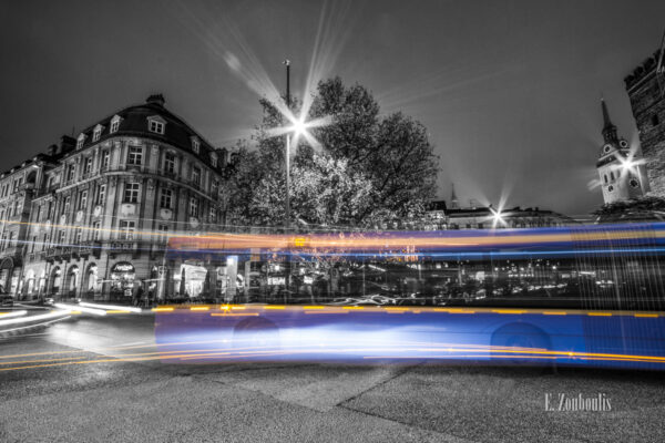 Schwarzweiß Aufnahme bei Nacht in München. Im Vordergrund der farbige Lichtschweif, der einen Bus der Linie 62 erkennen lässt und im Hintergrund die schöne Architektur des alten Gebäude und der Turm der Peterskirche (St. Peter)