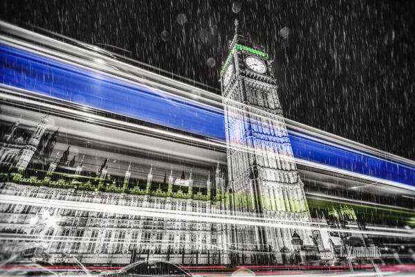 Schwarzweiß Aufnahme bei Nacht vor dem Big Ben in London mit einem farbigen Lichtschweif, der am Palace of Westminster bei strömendem Regen vorbeizieht und den Verkehr sichtbar macht