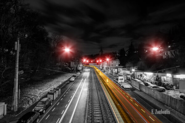 Schwarzweiß Aufnahme bei Nacht in Stuttgart Kaltental. Ein gelber Lichtschweif einer vorbeifahrenden Straßenbahn ist entlang der Schienen zu sehen. Der Frost hat sich auf der Straße abgesetzt. Roter Farbeffekt, die die Straßenbeleuchtung kennzeichnen