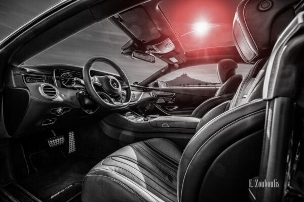 Schwarzweiß Aufnahme mit roten Elementen eines schwarzen Mercedes AMG S63 vor der Burg Hohenzollern. Blick in das Interieur der S-Klasse Durch das Fenster sieht man die Burg. Aufnahme entstanden auf Einladung von Mercedes Benz