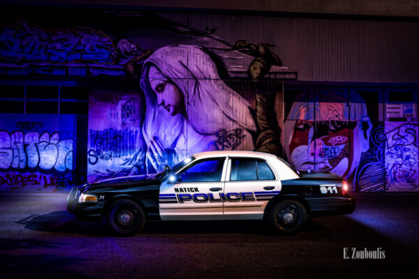 Amerikanisches Polizei Auto im Einsatz. Im Hintergrund ein Graffitti Bild eine Graffitti Wand mit einer betenden Frau von Dingo Babusch