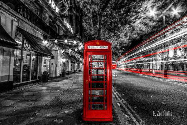 Schwarzweiß Aufnahme bei Nacht in Aldwych, London mit einer roten Telefonzelle und roten Lichtschweifen, die den vorbeifahrenden Verkehr zeigen