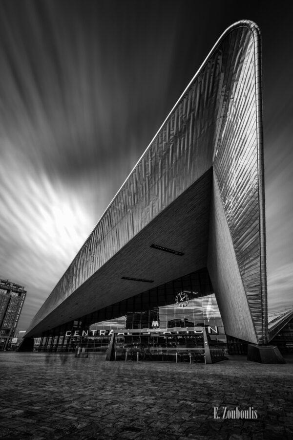 Schwarzweiss-Aufnahme am Hauptbahnhof in Rotterdam, Niederlande. Blick auf die vorbeiziehenden Wolken am Himmel hinter dem Gebäude am Bahnhof