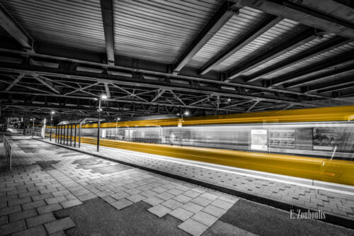 Schwarzweiß-Aufnahme am Nordbahnhof Stuttgart. Die vorbeifahrende Stadtbahn hinterlässt einen gelben Lichtschweif