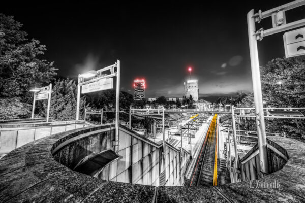 Schwarzweiß-Aufnahme am Pragsattel in Stuttgart. Blick auf einem im Vordergrund aus dem Tunnel kommenden gelben Lichtschweif einer Straßenbahn. Im Hintergrund befindet sich der Hochbunker und links davon das Hochhaus 'Skyline Stuttgart'