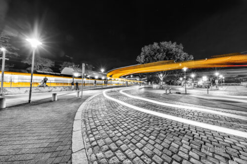 Schwarzweiß-Aufnahme am Bahnhof in Stuttgart-Feuerbach mit gelben Lichtschweifen von ein- und ausfahrenden Straßenbahnen und Bussen
