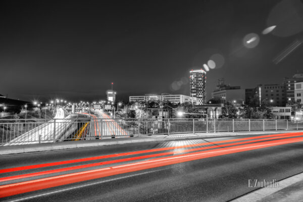 Schwarzweiss-Aufnahme am Pragsattel in Stuttgart. Der vorbeiziehende Verkehr hinterlässt farbige Lichtschweife. Im Hintergrund ist der Hochbunker und das Gebäude der Mercedes Benz Bank vor dem Skyline-Hochhaus zu sehen