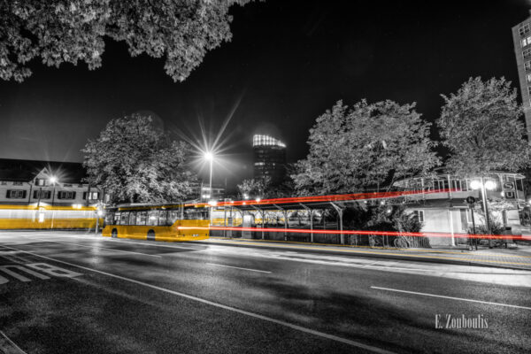 Schwarzweiss-Aufnahme am Bahnhof in Stuttgart Vaihingen. Im Vordergrund fährt ein Bus ein und zieht einen roten und gelben Lichtschweif hinter sich. Die Straßenbahn verlässt den Bahnhof in Lichtgeschwindigkeit. Im Hintergrund sieht man den Colorado Turm