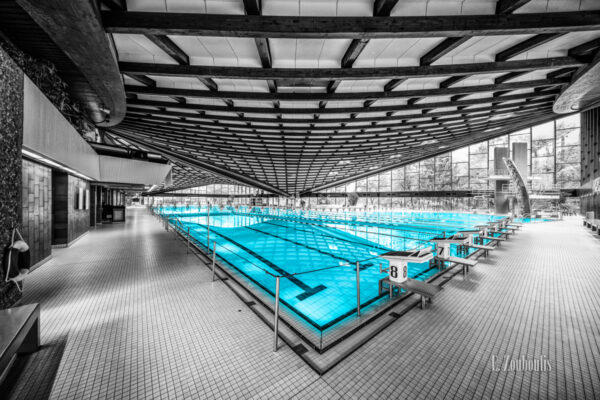 Schwarzweiß Aufnahme im Inneren des Badezentrum Sindelfingen. Das Wasser in den Becken ist in blau zu sehen. Seitliche Ansicht über Eck auf das 50m Becken.