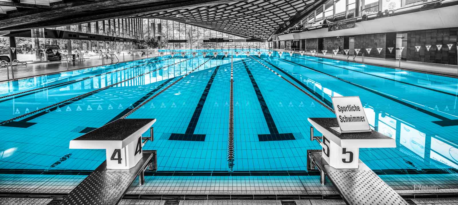 Schwarzweiß Aufnahme im Inneren des Badezentrum Sindelfingen. Das Wasser in den Becken ist in blau zu sehen. Frontal-Ansicht auf das 50m Becken. Im Hintergrund ist der Sprungturm zu sehen