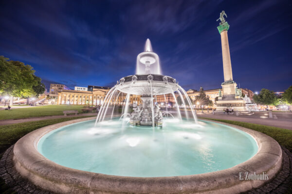 Bild vom Schloßplatzspringbrunnen in Stuttgart am Schlossplatz bei Nacht. Rechts im Bild ist die Jubiläumssäule zu sehen. Im Hintergrund befindet sich der Königsbau.