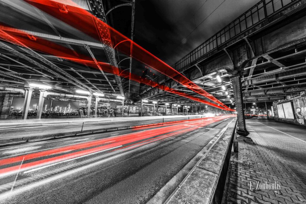 Nachtaufnahme von Frankfurt am Main an der Hanauer Straße unter einer Brücke in Ostend. Im Hintergrund ist das Gebäude der EZB zu sehen. Im Vordergrund zeigt sich durch die eingefärbten Light-Trails die Dynamik von FFM bei Nacht