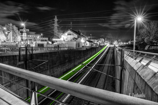 Nachtaufnahme in Holzgerlingen an der Böblinger Str. bei Böblingen. Blick auf die Gleise während ein Zug vorbeifährt und eine grüne Lichtspur hinterlässt