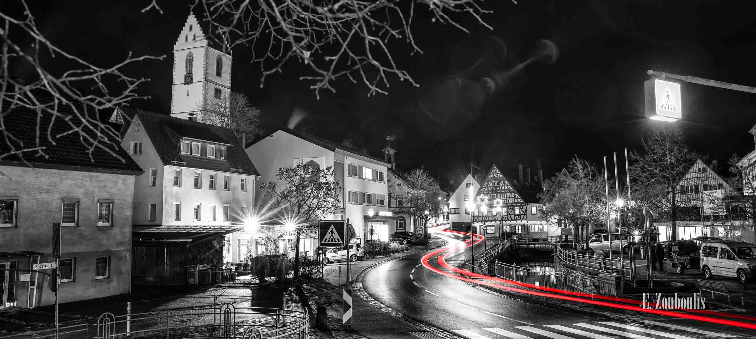 Nachtaufnahme in Aidlingen bei Böblingen. Zu sehen ist neben der Aid, die Hauptstraße und die roten Lichtschweife, die den Verkehr kennzeichnen. Im Hintergrund steigt der Kirchenturm der evangelischen Kirchengemeinde empor