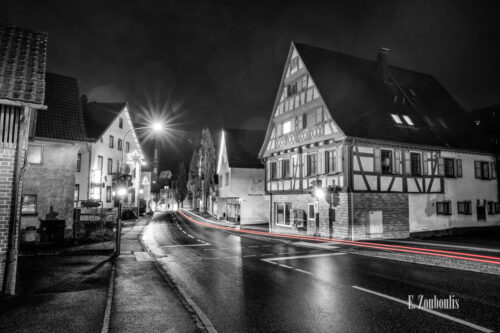 Nachtaufnahme in Aidlingen bei Böblingen. Zu sehen ist die Hauptstraße auf der einige Fachwerkhäuser zu finden sind. Davor sind rote Lichtschweife, die den Verkehr kennzeichnen