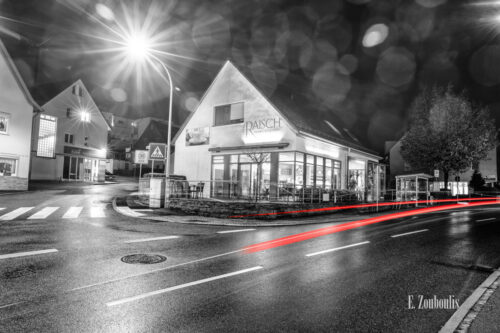 Nachtaufnahme in Aidlingen bei Böblingen. Zu sehen ist die Hauptstraße und die Bäckerei Raisch. Davor sind rote Lichtschweife, die den Verkehr kennzeichnen