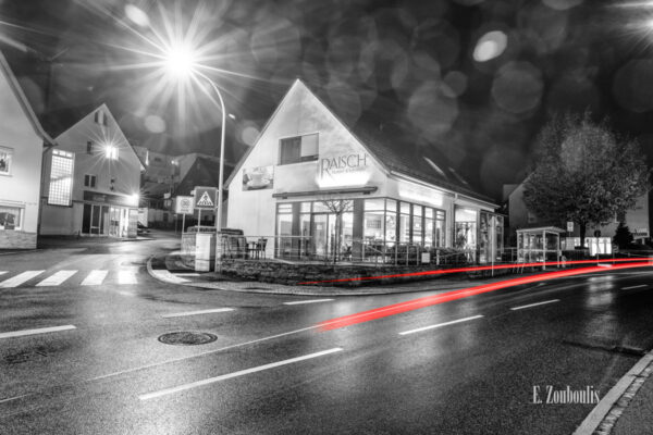 Nachtaufnahme in Aidlingen bei Böblingen. Zu sehen ist die Hauptstraße und die Bäckerei Raisch. Davor sind rote Lichtschweife, die den Verkehr kennzeichnen