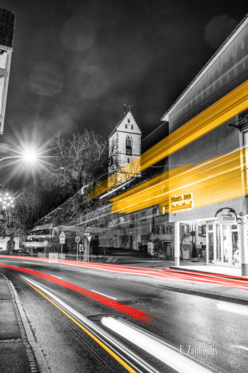 Nachtaufnahme in Aidlingen bei Böblingen. Zu sehen ist die Hauptstraße und das Haus am Zehnthof. Davor sind rote Lichtschweife, die den Verkehr kennzeichnen. Im Hintergrund steigt der Kirchenturm der evangelischen Kirchengemeinde empor