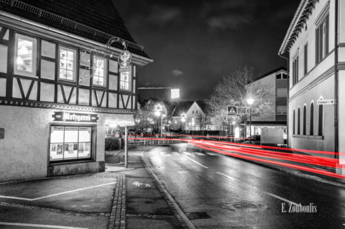 Nachtaufnahme in Aidlingen bei Böblingen. Zu sehen ist die Hauptstraße und die Bäckerei Raisch. Davor sind rote Lichtschweife, die den Verkehr kennzeichnen