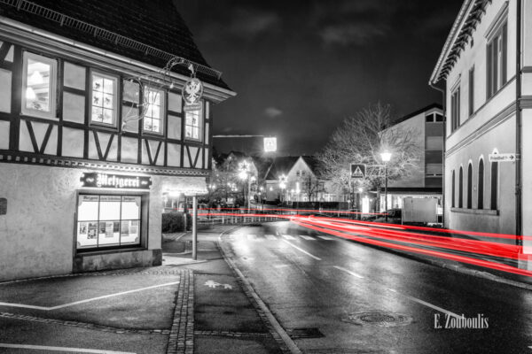 Nachtaufnahme in Aidlingen bei Böblingen. Zu sehen ist die Hauptstraße und die Bäckerei Raisch. Davor sind rote Lichtschweife, die den Verkehr kennzeichnen