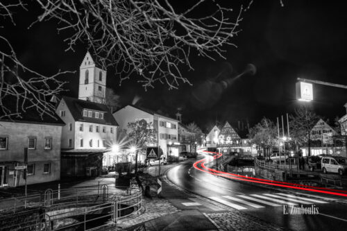 Nachtaufnahme in Aidlingen bei Böblingen. Zu sehen ist neben der Aid, die Hauptstraße und die roten Lichtschweife, die den Verkehr kennzeichnen. Im Hintergrund steigt der Kirchenturm der evangelischen Kirchengemeinde empor