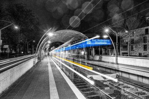 Nachtaufnahme an der Haltestelle Ollenhauerstraße in Bonn bei Nacht. Zu sehen ist eine einfahrende Straßenbahn der SWB Richtung Bad Godesberg mit blauen und gelben Licht Trails.
