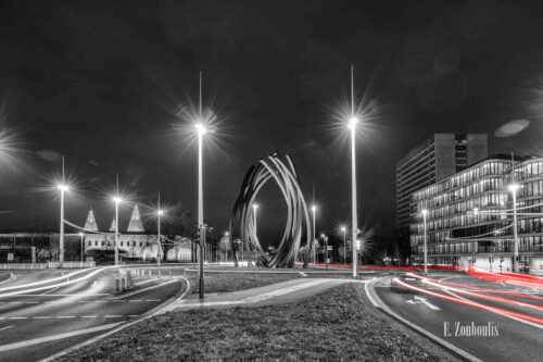 Nachtaufnahme am Helmut-Schmidt-Platz in Bonn bei Nacht. Zu sehen ist der nächtliche Verkehr, der an der Skulptur Arc'89 von Bernar Venet am Kreisverkehr vorbeizieht und rote Light Trails hinterlässt