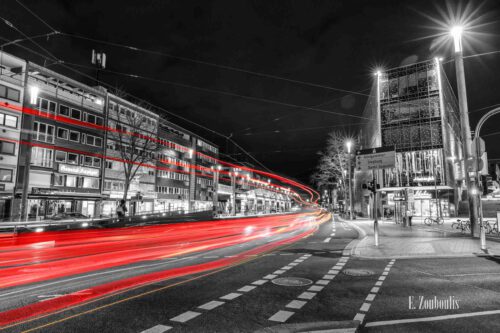 Nachtaufnahme am Konrad-Adenauer-Platz in Bonn bei Nacht. Zu sehen ist der nächtliche Verkehr, der an der gleichnamigen Haltestelle vorbeizieht und rote Light Trails hinterlässt